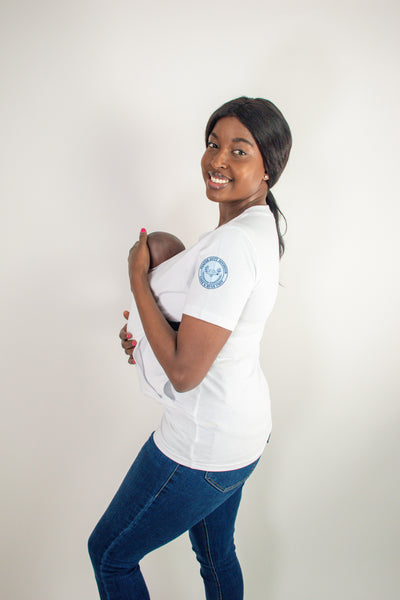 White baby carrier t-shirt worn by a woman standing up smiling and looking at camera with baby